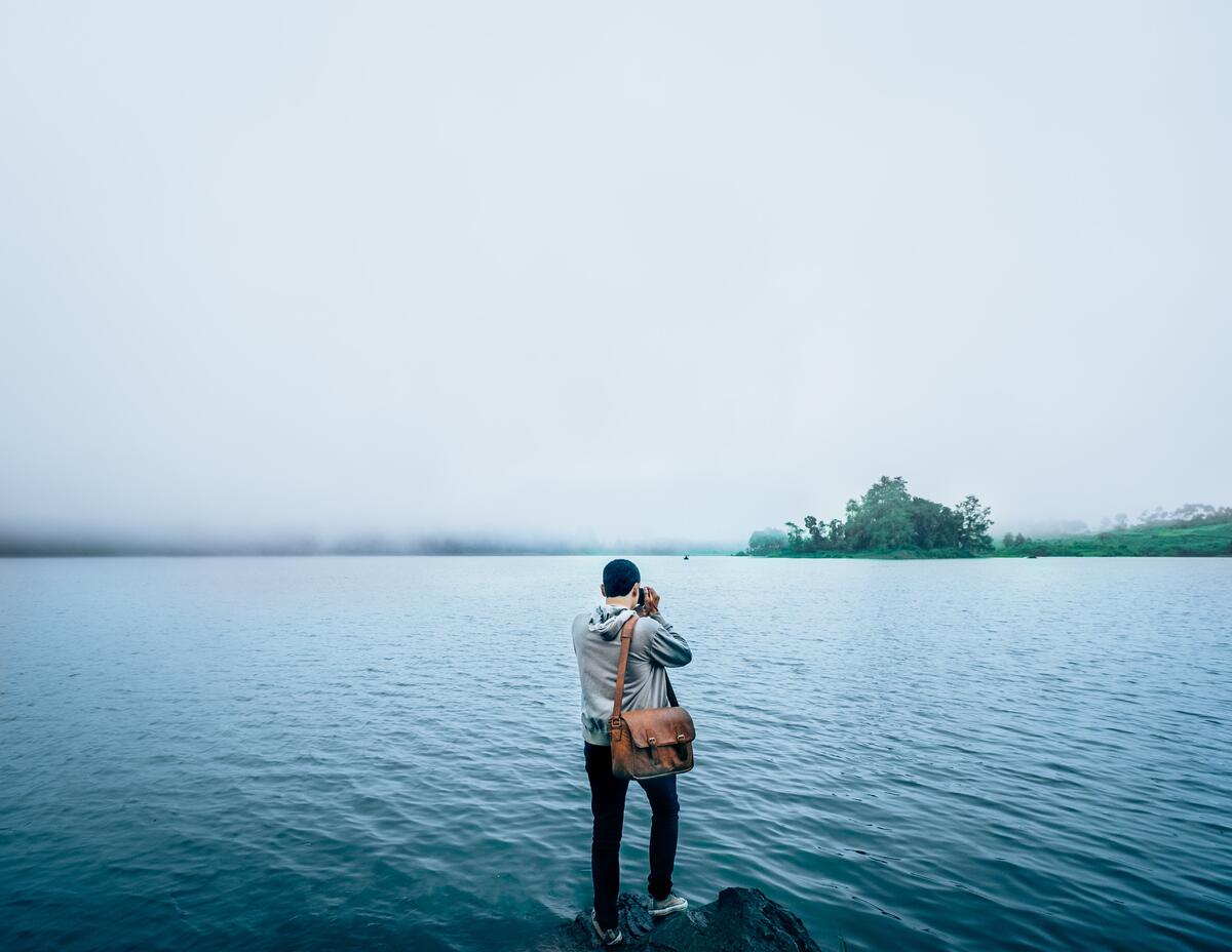 Мужчина фотографирует утреннее туманное озеро