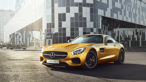 A yellow Mercedes AMG GTR stands in front of a house on a sunny street