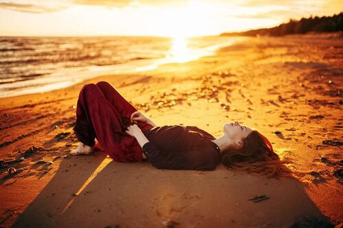 Девушка в вечернем костюме лежит на песчаном пляже и наслаждается солнечным закатом