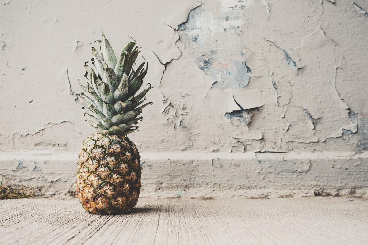 Pineapple lying on the floor against an old wall with peeling paint