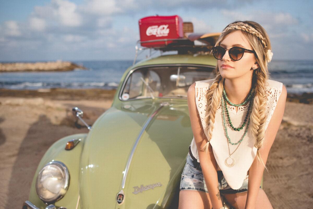 A girl sits on the hood of a Volkswagen Beetle