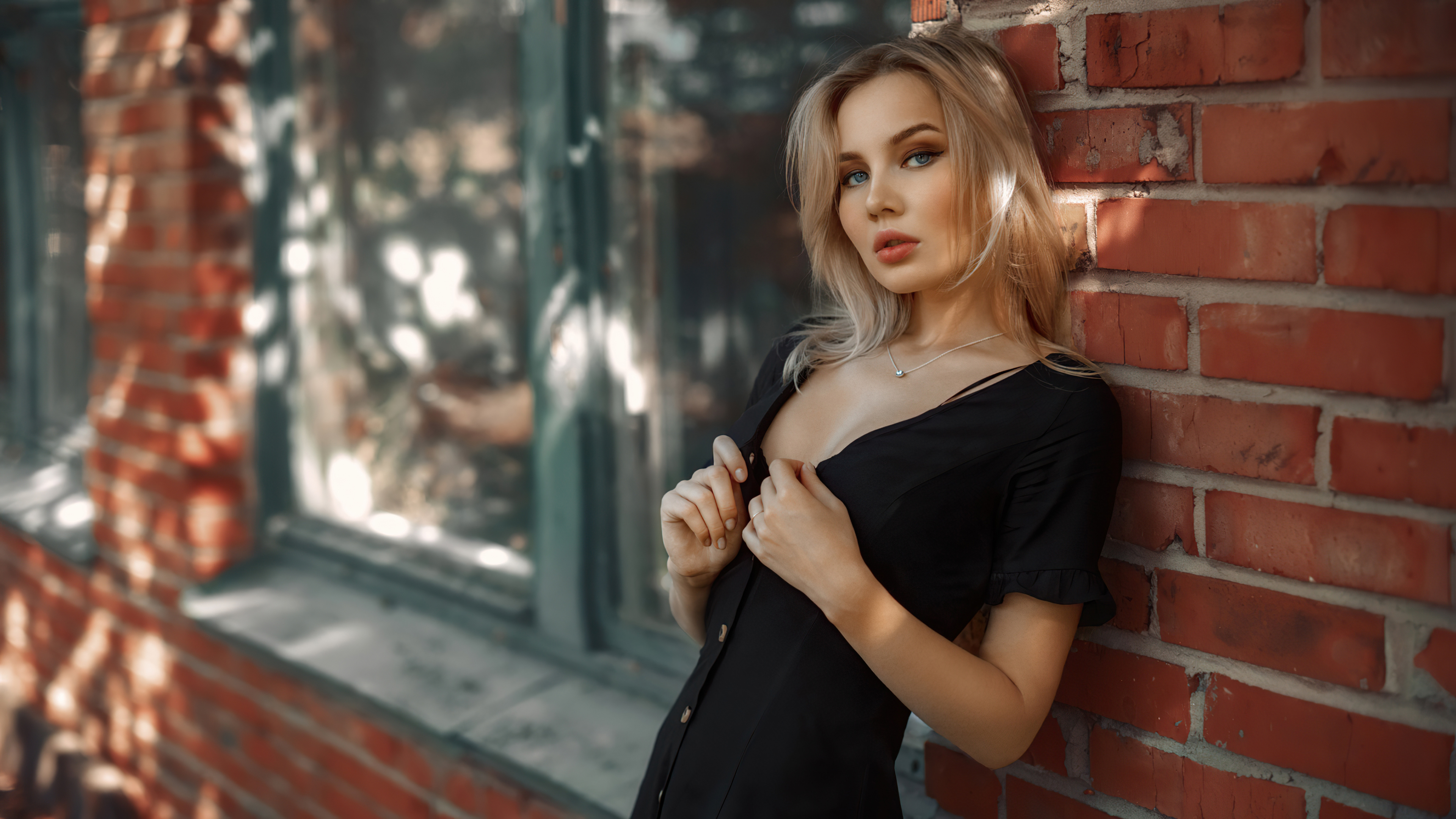 Голубоглазая блондинка в черном платье стоит у красной кирпичной стены