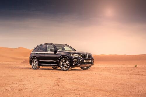 A black BMW X3 in the desert under the blazing sun.