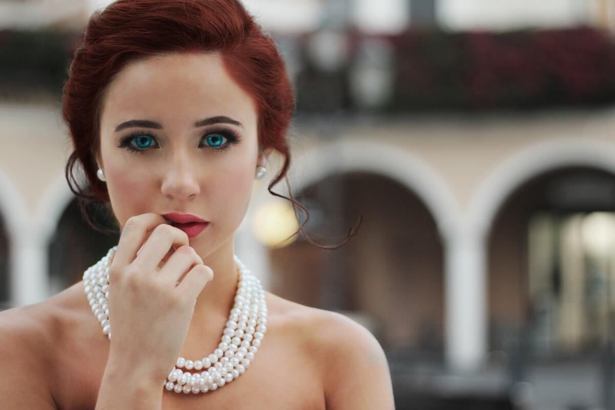Red-haired girl with blue eyes and white beads on her bare neck