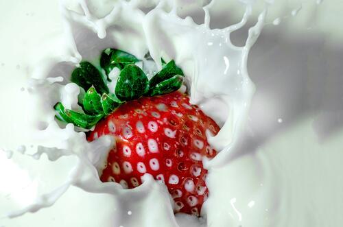 A strawberry falls into the liquid yogurt