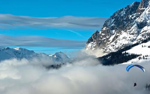 Парашютист пролетает над облаками в горах
