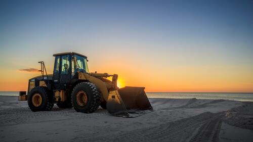 一辆拖拉机正在平整海边新海滩上的沙地。