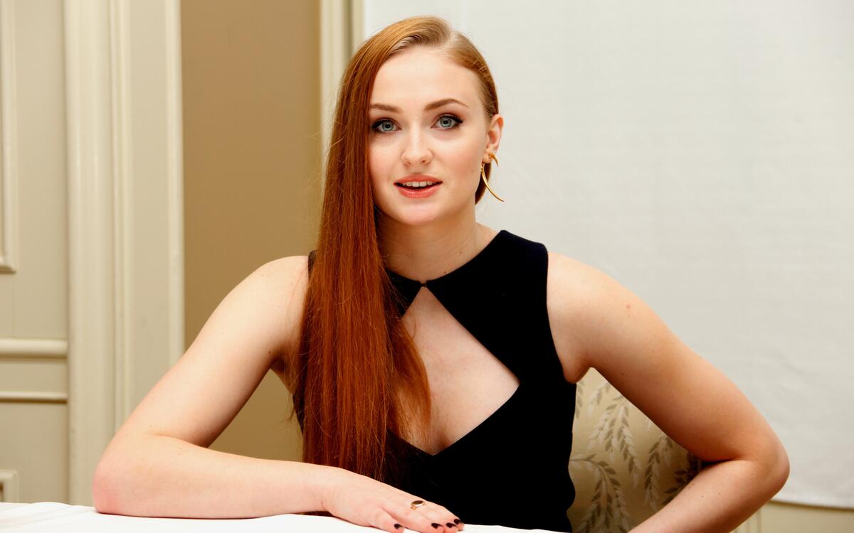 A red-haired Sophie Turner sits at her desk.