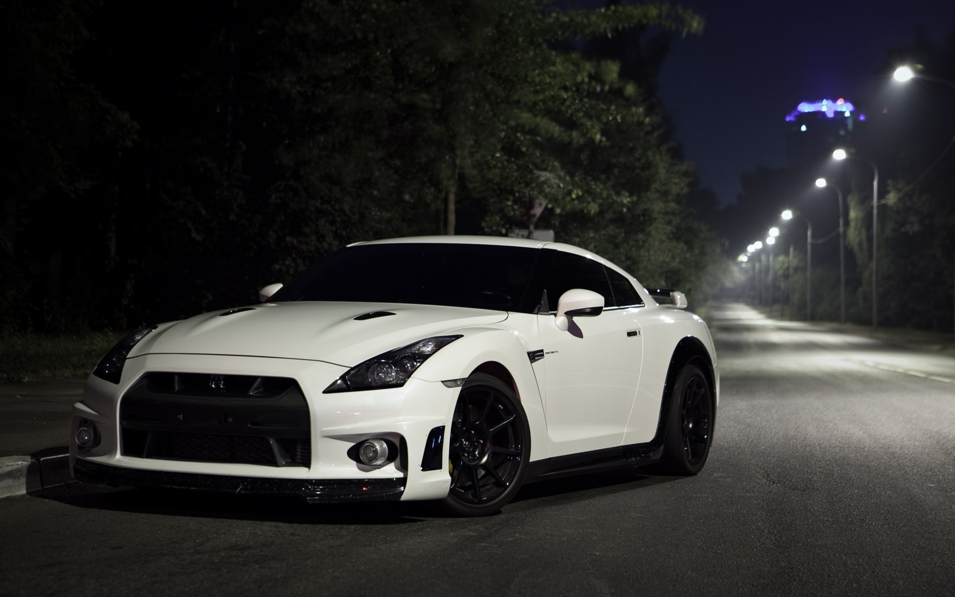 A white nissan gtr stands under the night lights.