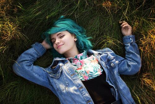 A happy girl with blue hair lying in the grass