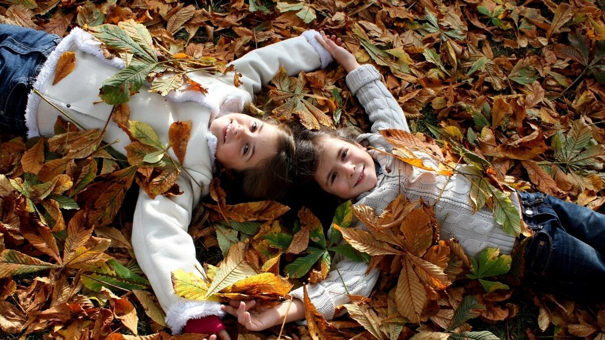 Дети лежат на осенних листьях