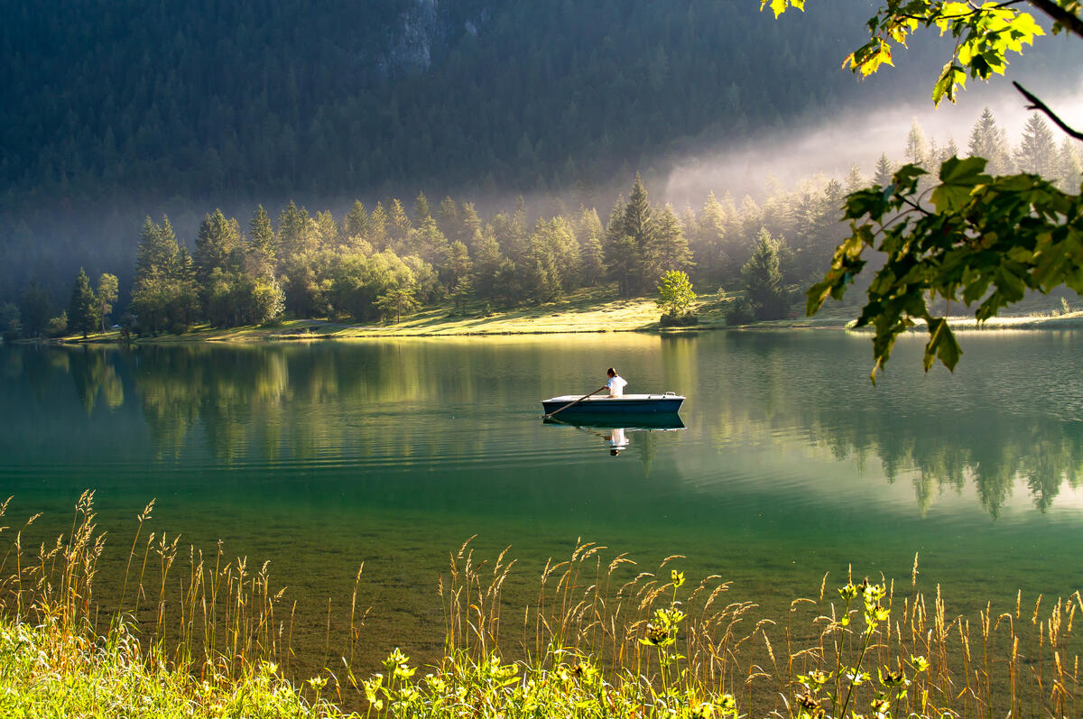 A fisherman on a boat floating on a clear river in the mountains