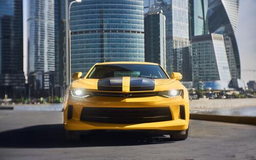 Yellow Chevrolet Camaro with black stripes on the hood on the background of Moscow City skyscraper