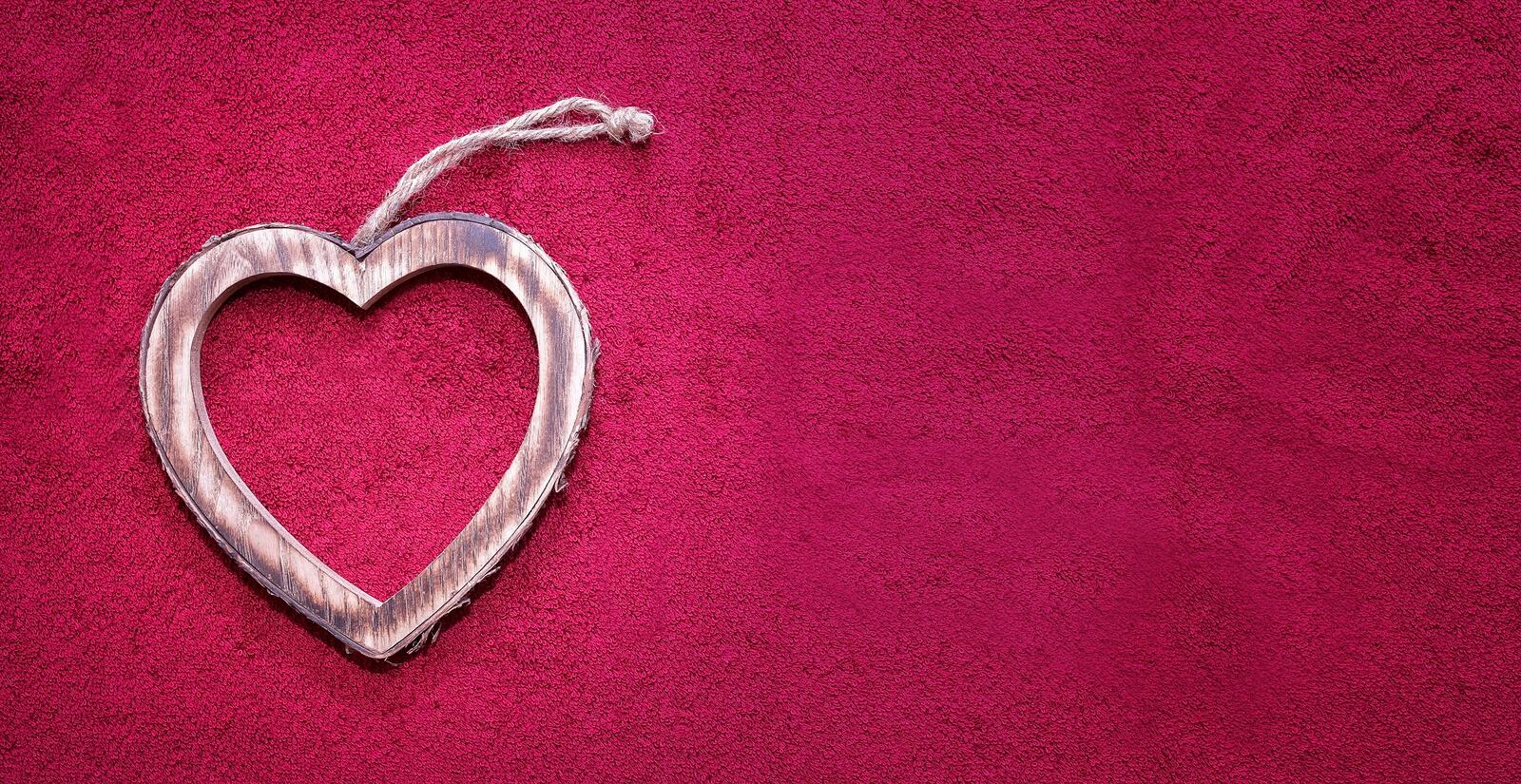 Free photo Wooden keychain in the shape of a heart on a pink background