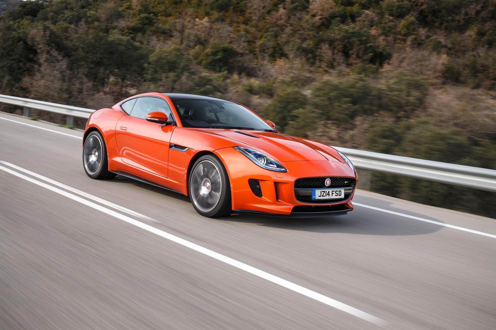 Free photo A bright orange Jaguar F Type driving down a country road.