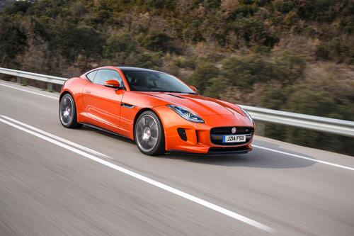 A bright orange Jaguar F Type driving down a country road.
