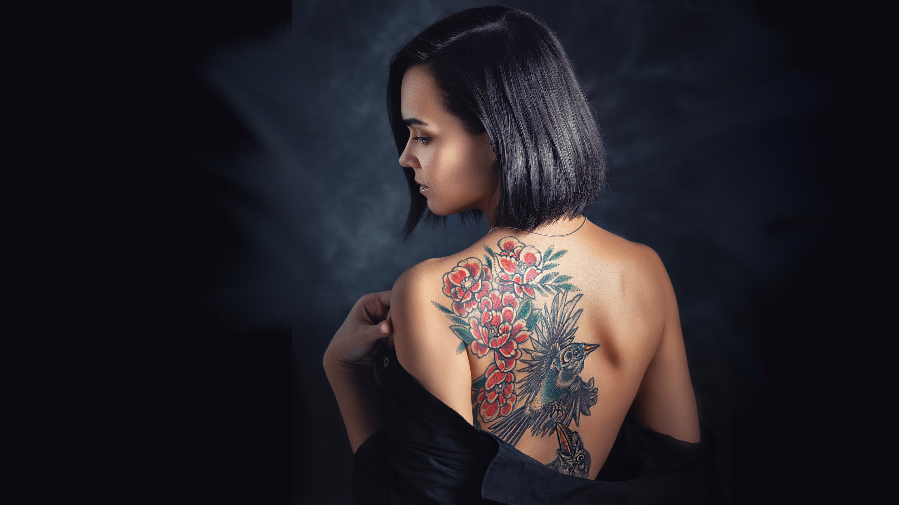 Красивая темноволосая девушка с короткими волосами демонстрирует татуировку на спине