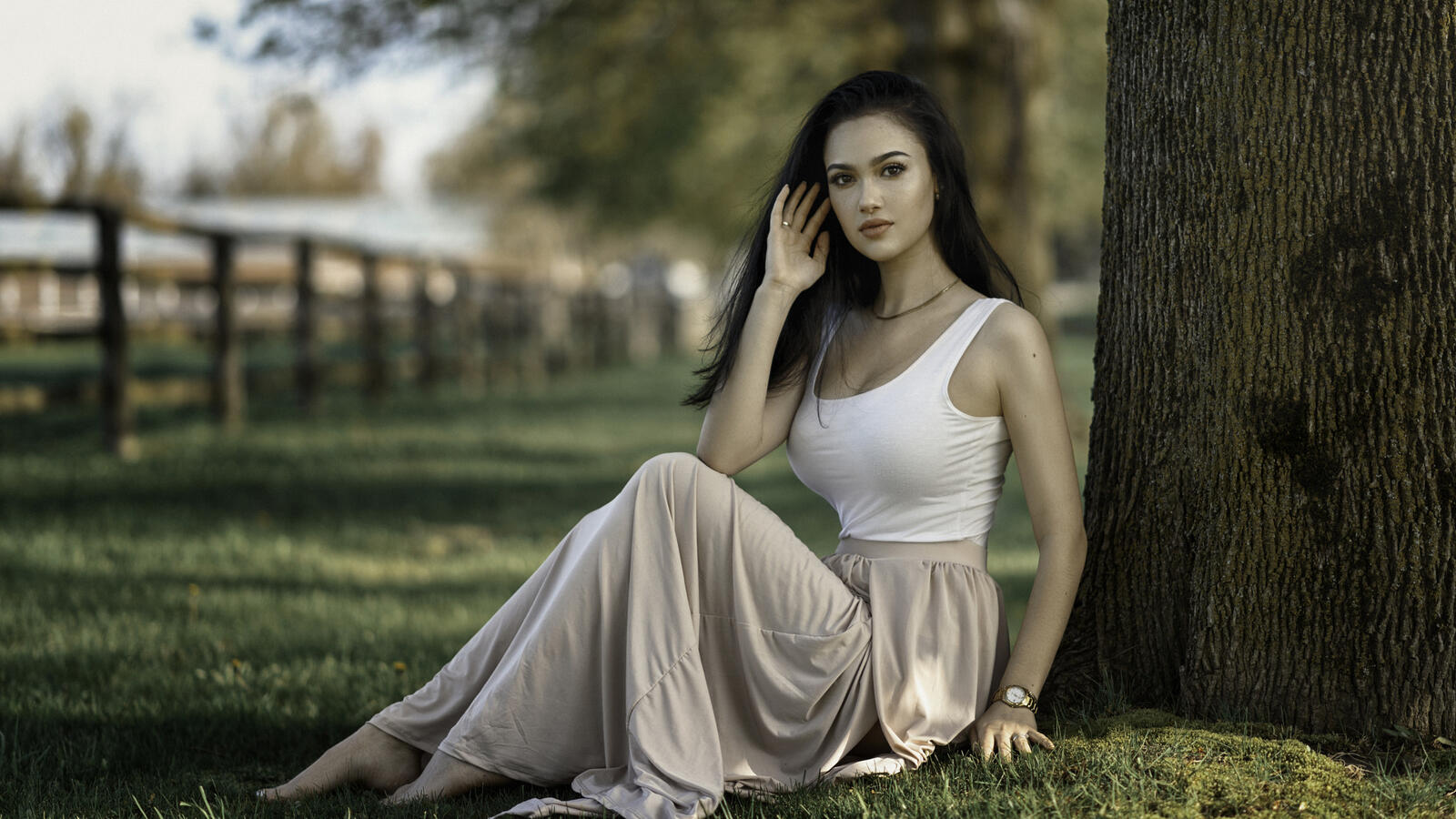 Free photo A dark-haired girl in a light skirt sits by a tree
