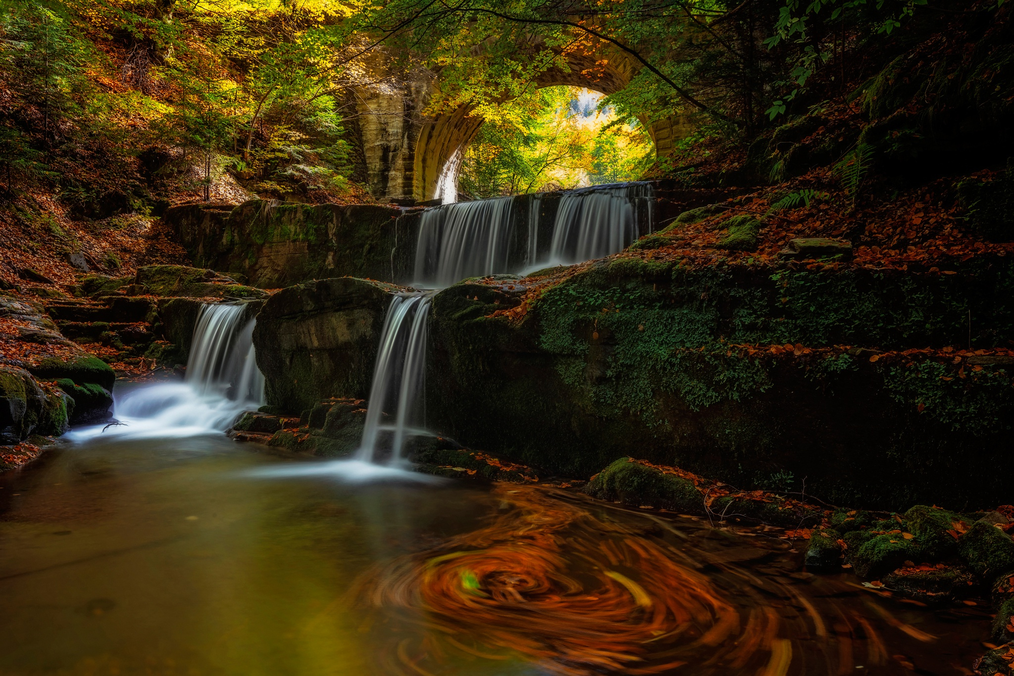 A waterfall with an arch in the fall woods