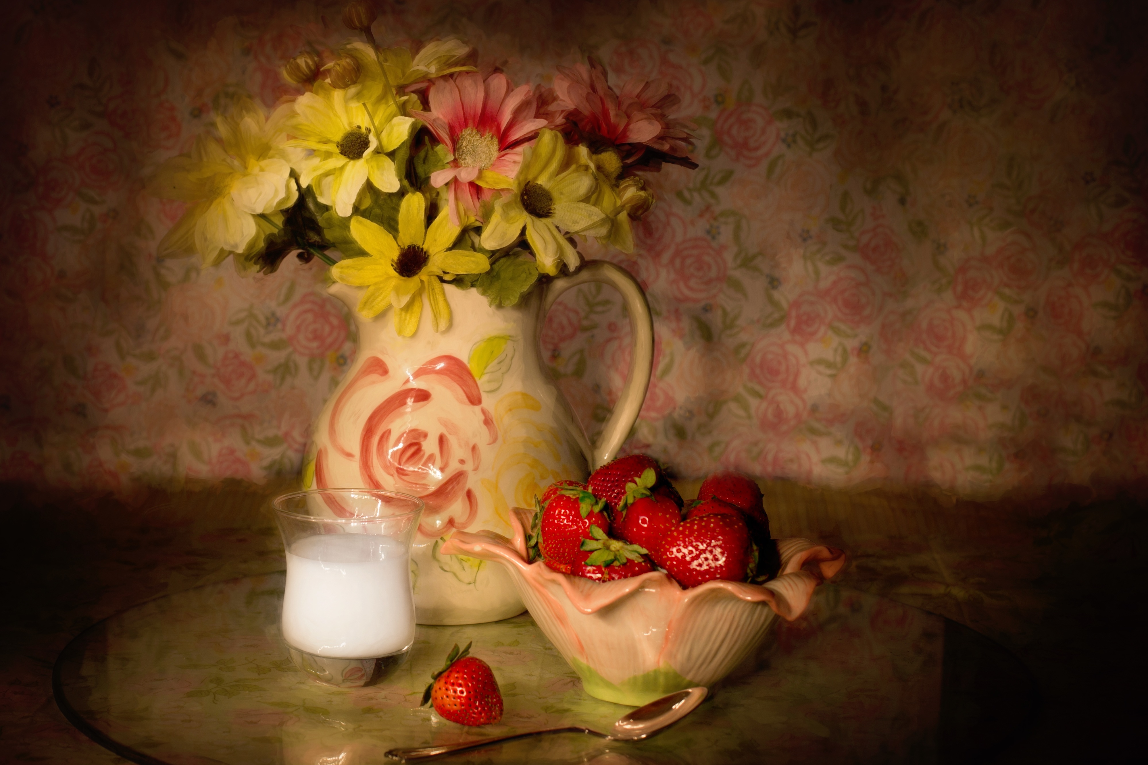 Flowers in a pitcher on a table with strawberries.