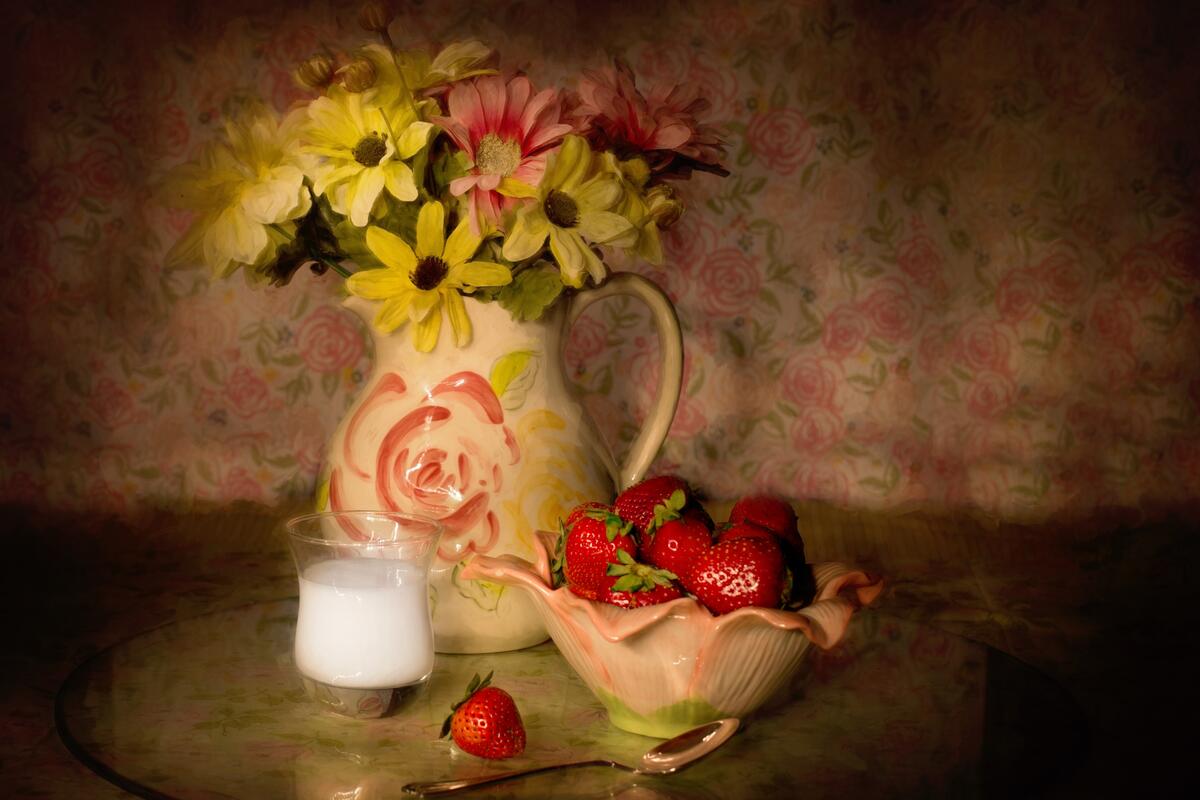 Flowers in a pitcher on a table with strawberries.