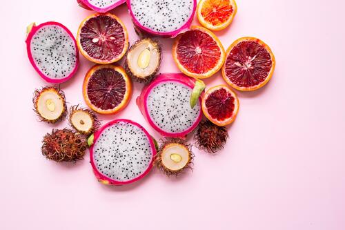 Экзотические фрукты рамбутан с питайя на розовом фоне