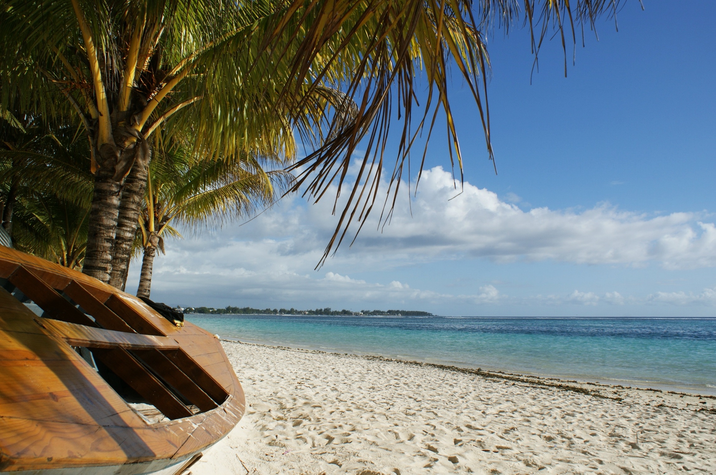 Деревянная лодка лежит на песчаном берегу под пальмами на солнечном свете