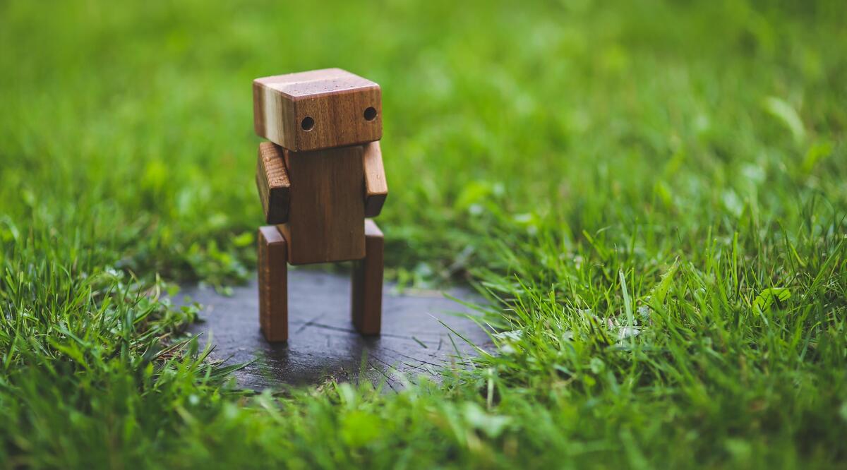 A small robot made of wood stands on a green lawn