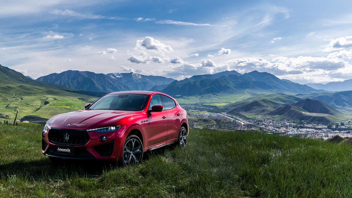 A red Maserati levante against the mountains.