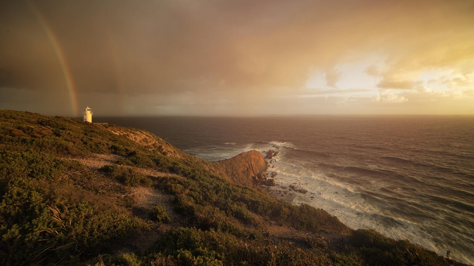 Free photo A rainbow over the ocean behind the lighthouse at daybreak