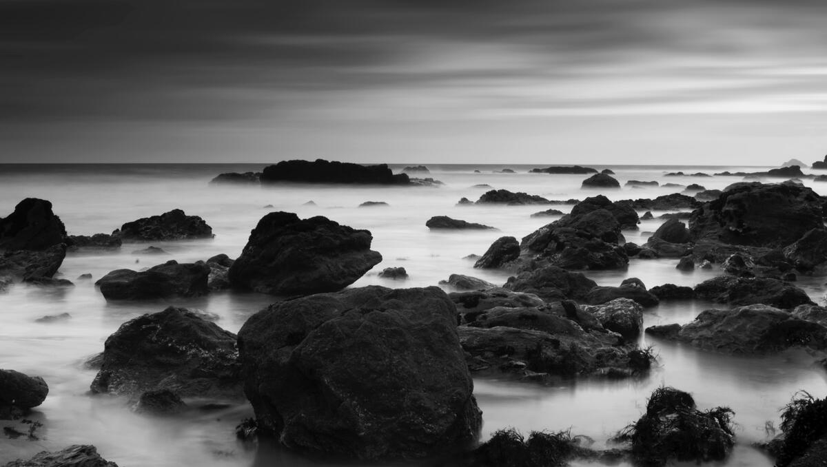 Black and white photo of the sea shore with rocks