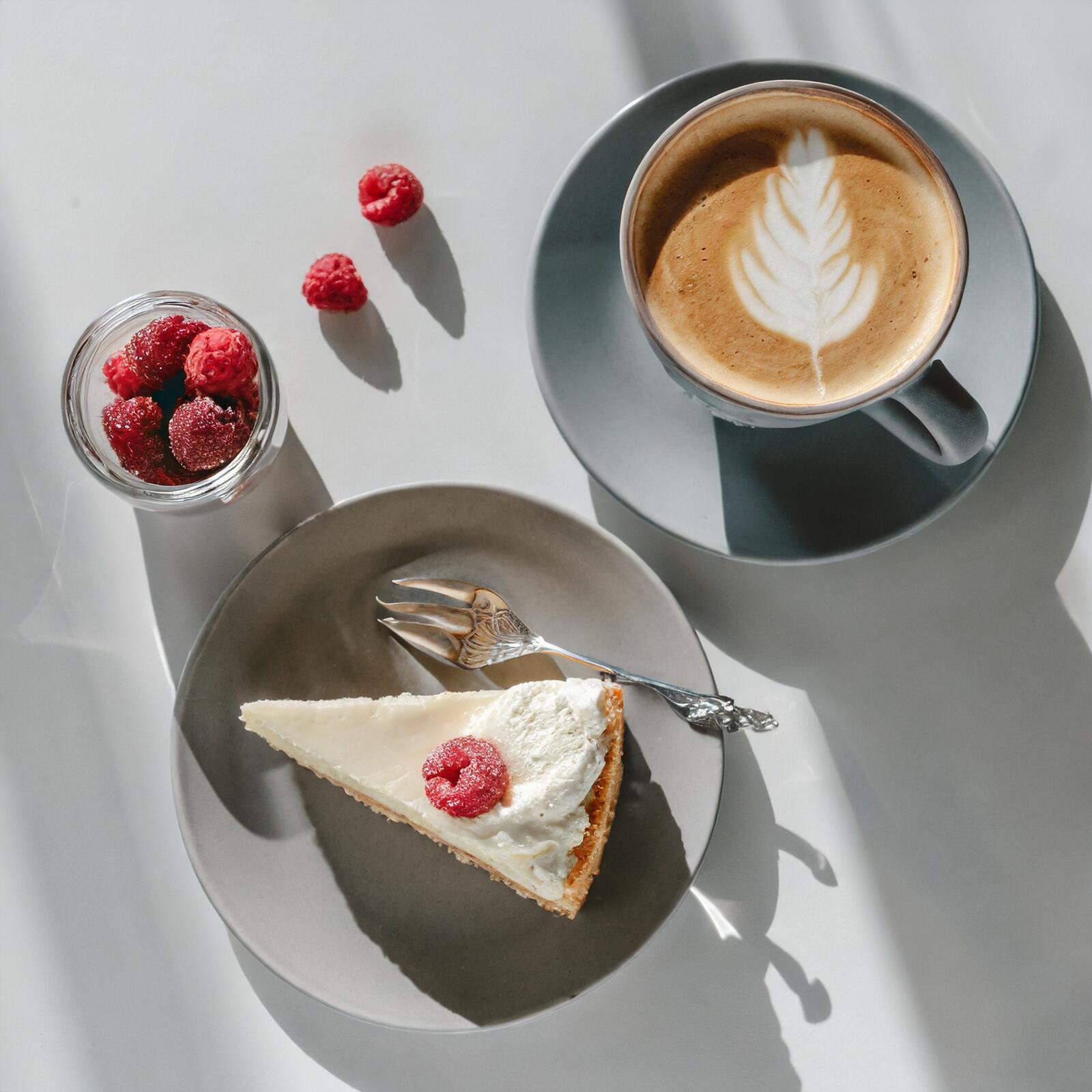 Free photo A white coffee cup next to a plate with a slice of cake on it