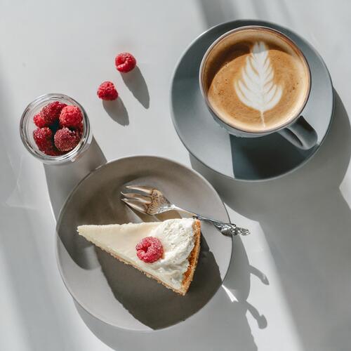 Белая чашка кофе рядом с тарелкой с кусочком торта