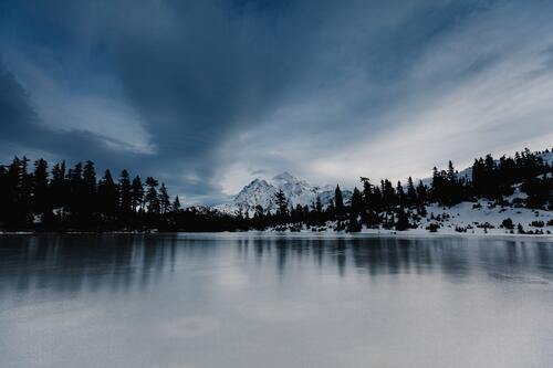 An ice-covered lake in the forest with a mountain.
