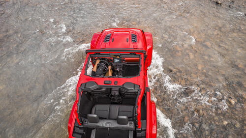 Red Jeep Wrangler Rubicon crosses a shallow river