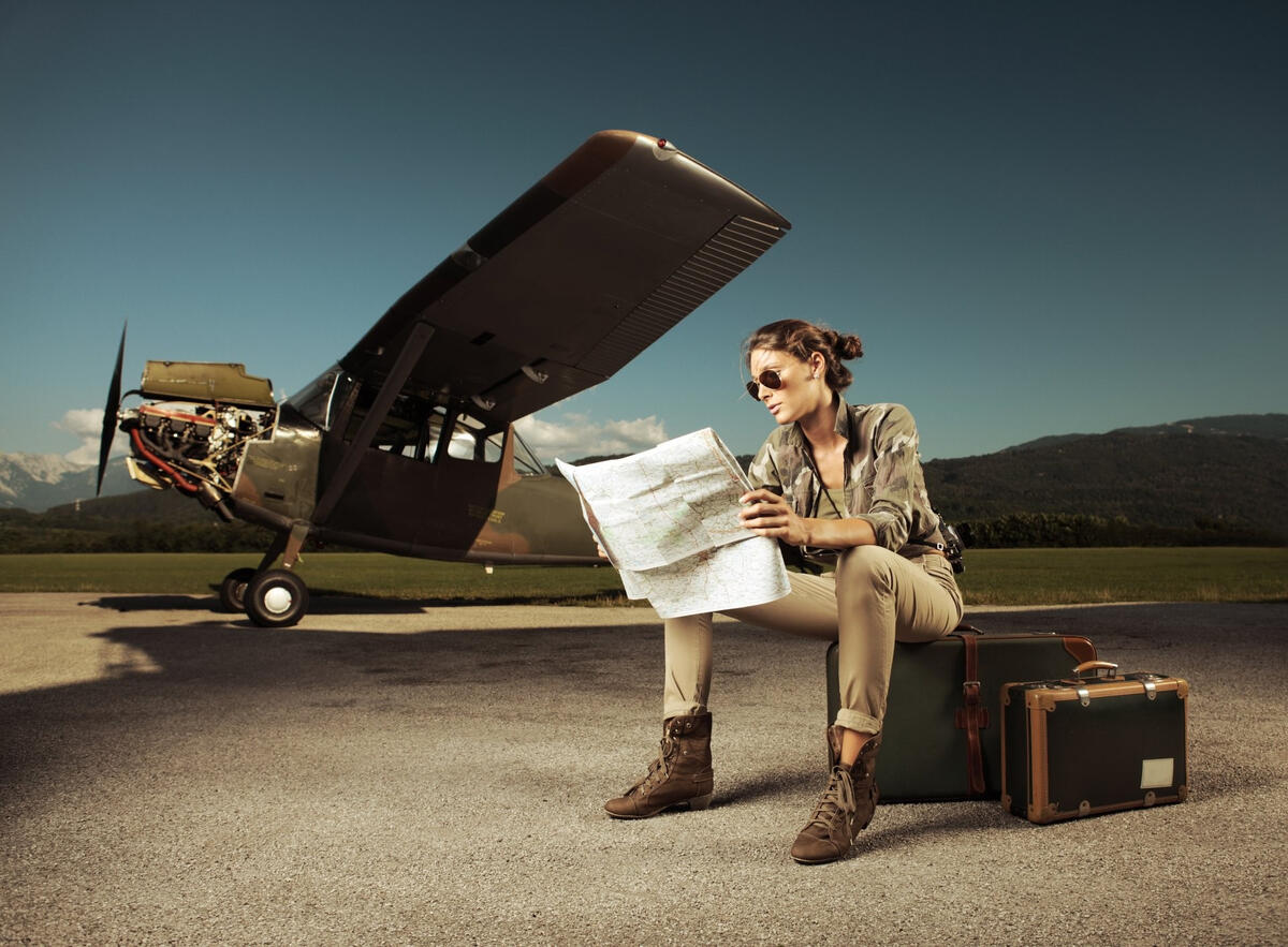 Девушка сидит ряжом с военным самолетом на чемоданах