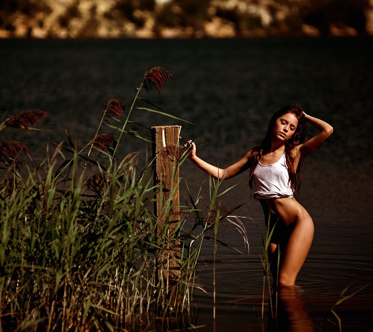 A girl in a wet T-shirt stands on the riverbank