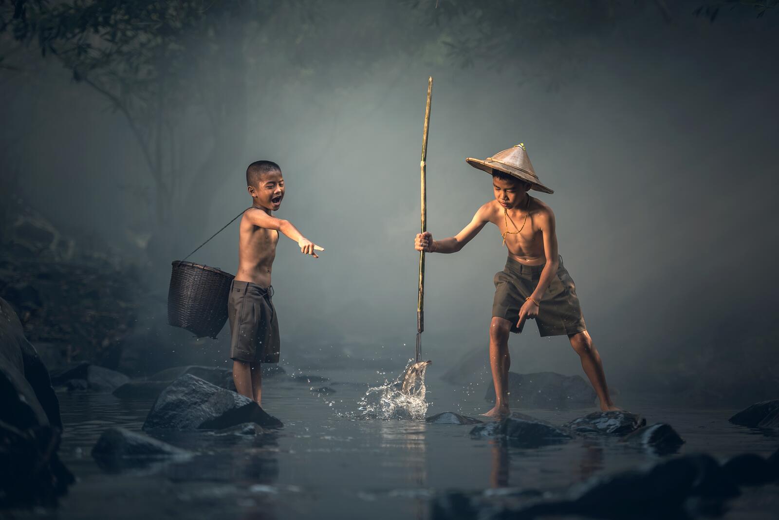 Бесплатное фото Два азиатских мальчика ловят рыбу копьем