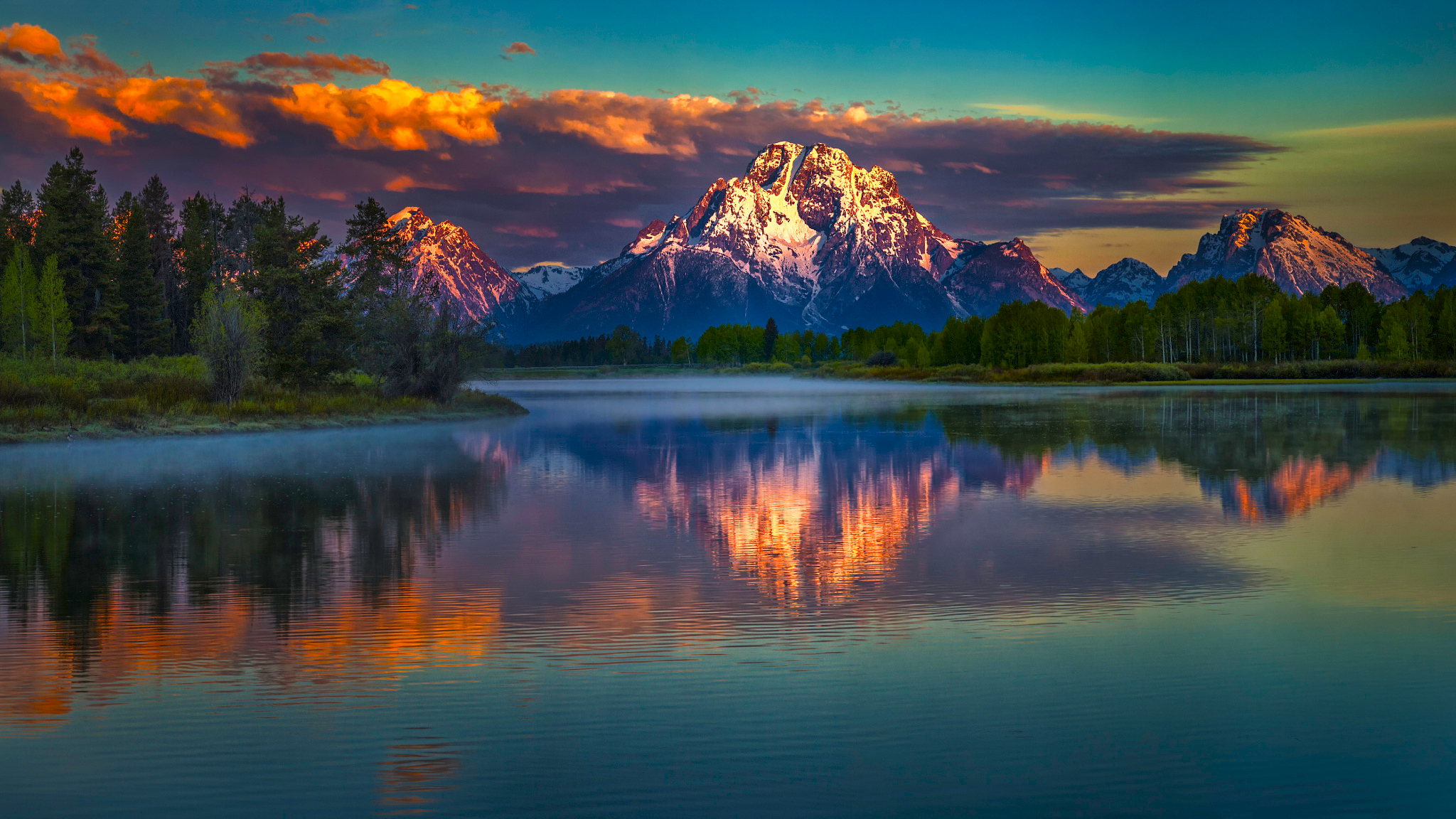 A mountain with a snowy peak is reflected in the lake at sunset