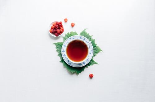 A mug of tea with raspberries on a light gray background