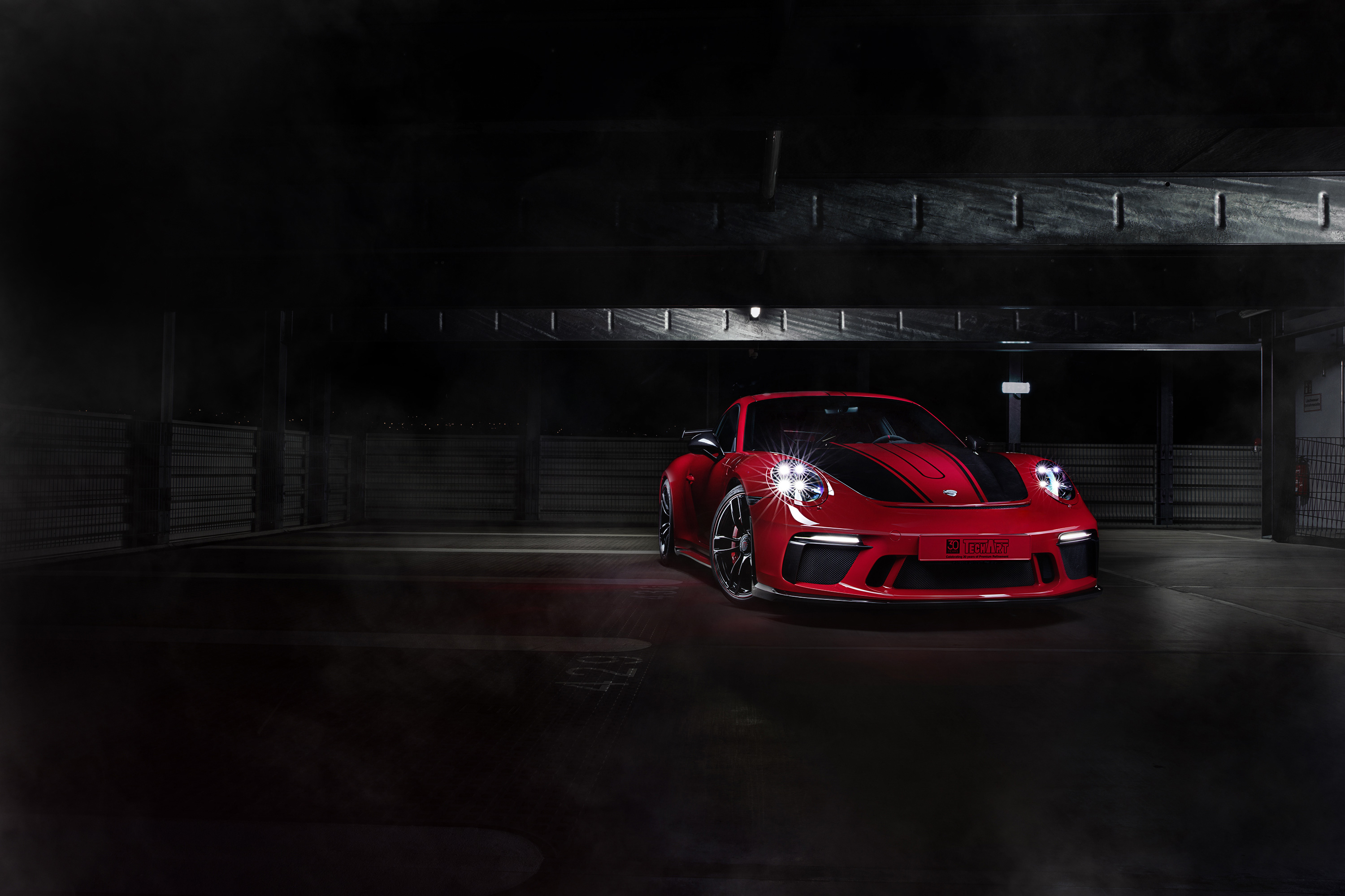 Красный с черными полосами Porsche 911 2018 года стоит в темном гараже