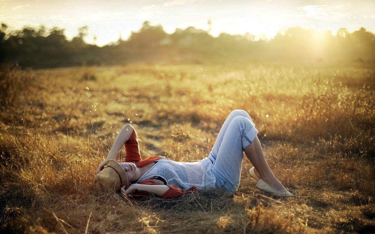 Девушка в шляпе лежит на полянке наслаждаясь солнечным светом