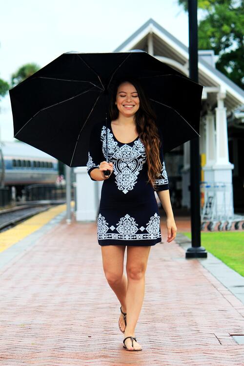 Beautiful girl in a dress hides from the sun under an umbrella