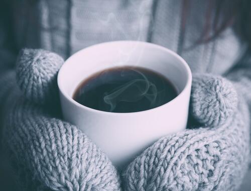 A cup of hot coffee in mittens.