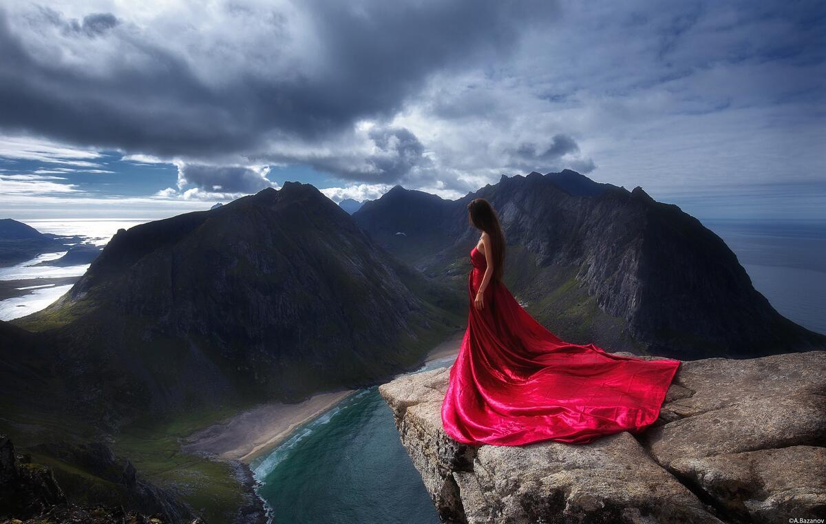 A girl in a long pink dress standing on a cliff.