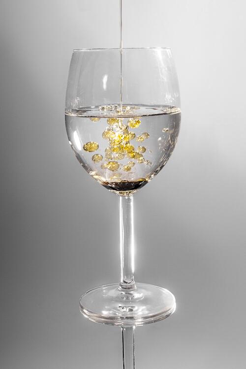 A glass with clear liquid and drops of oil