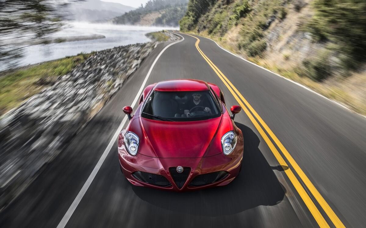Alfa romeo 4c в красном цвете едет по дороге на большой скорости
