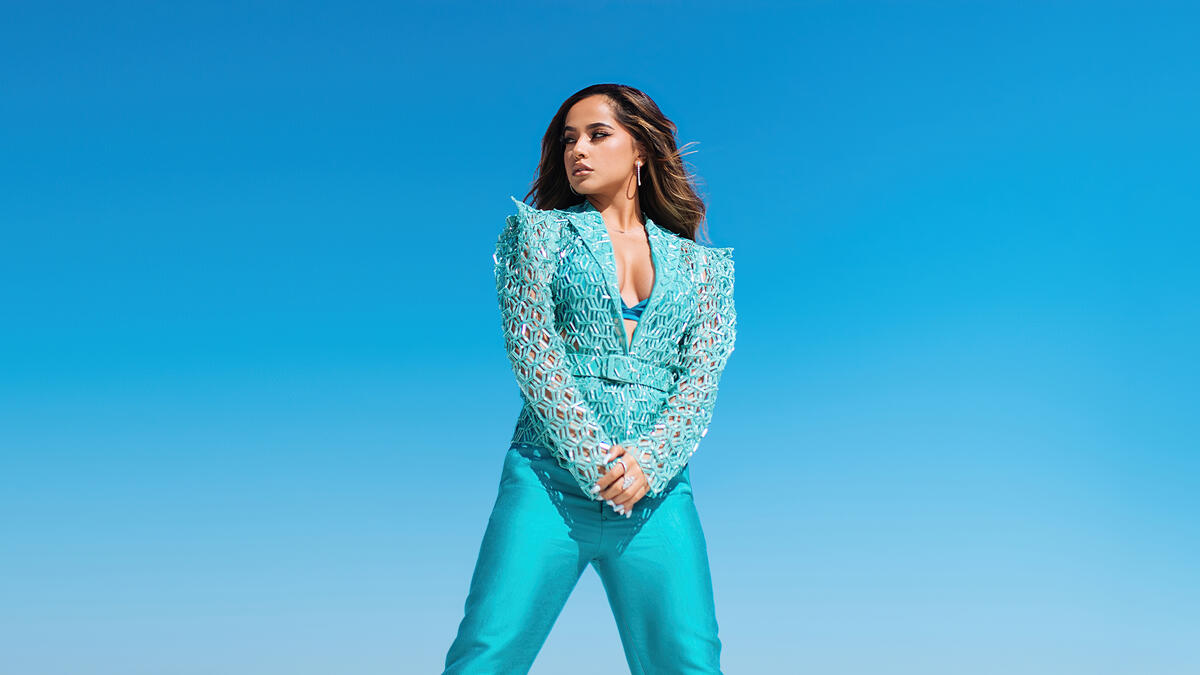 Becky G on a blue background in a blue suit