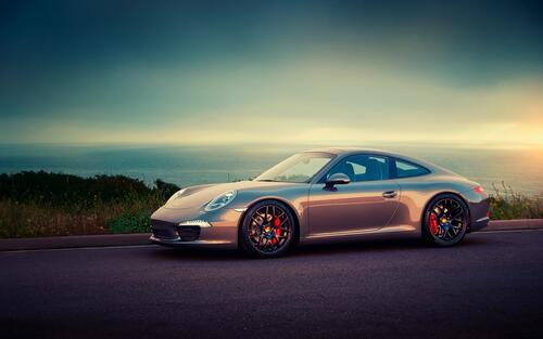 A gray Porsche 911 during sunset by the sea