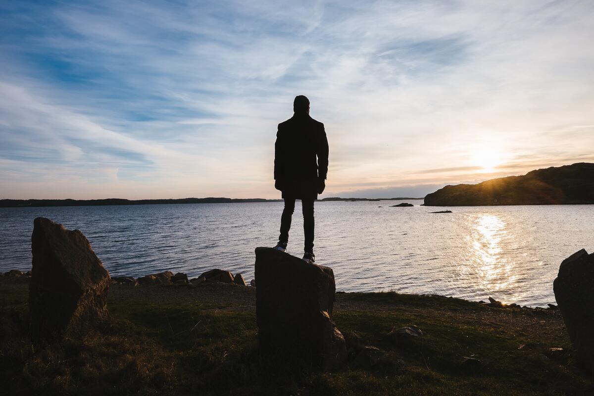 The silhouette of a man standing on a rock near the seashore